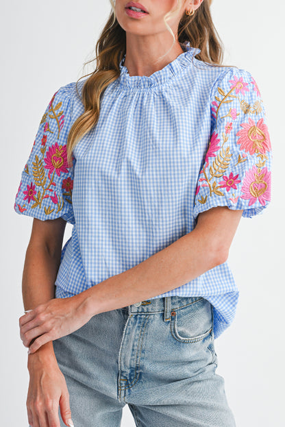 Woman wearing a blue checkered top with floral sleeves on a white background