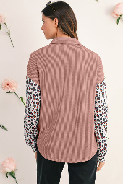 Woman wearing a ribbed brown shirt with leopard print sleeves against a light background with flowers.