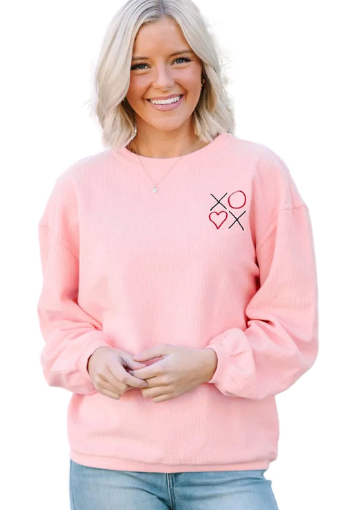Woman wearing a pink sweatshirt with a heart and cross design, standing in front of a white lattice background.