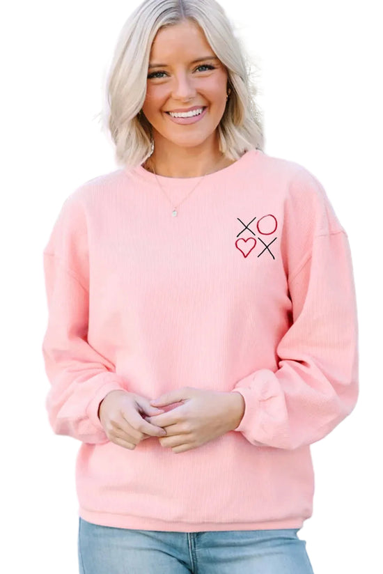 Woman wearing a pink sweatshirt with a heart and cross design, standing in front of a white lattice background.
