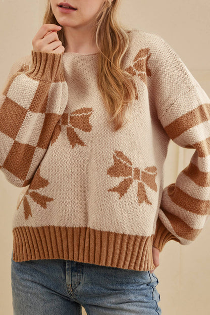 Person wearing a beige sweater with brown bow patterns and blue jeans.