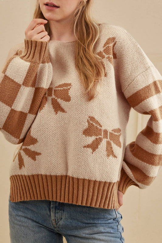 Person wearing a beige sweater with brown bow patterns and blue jeans.