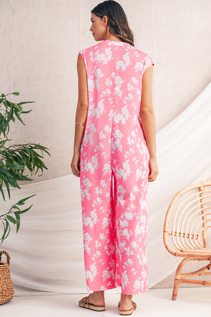 Woman wearing a pink floral jumpsuit standing in a minimalistic room with a plant and chair.