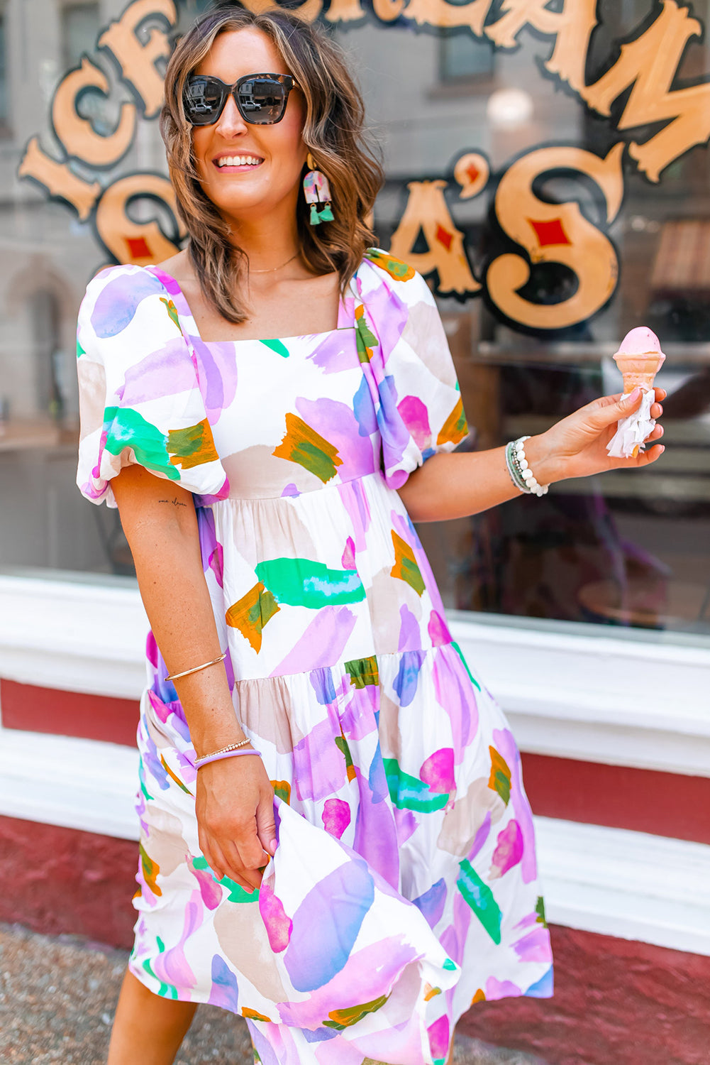 Front view of model wearing purple print dress with short bubble sleeves on a street setting.