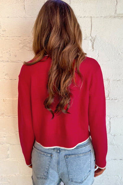 Person wearing a red sweater and light blue jeans against a white brick wall.