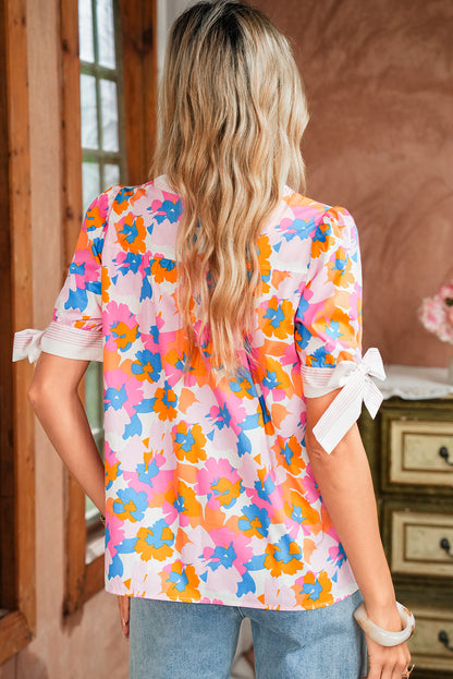 Woman wearing a colorful floral blouse with bows on the sleeves in an indoor setting.