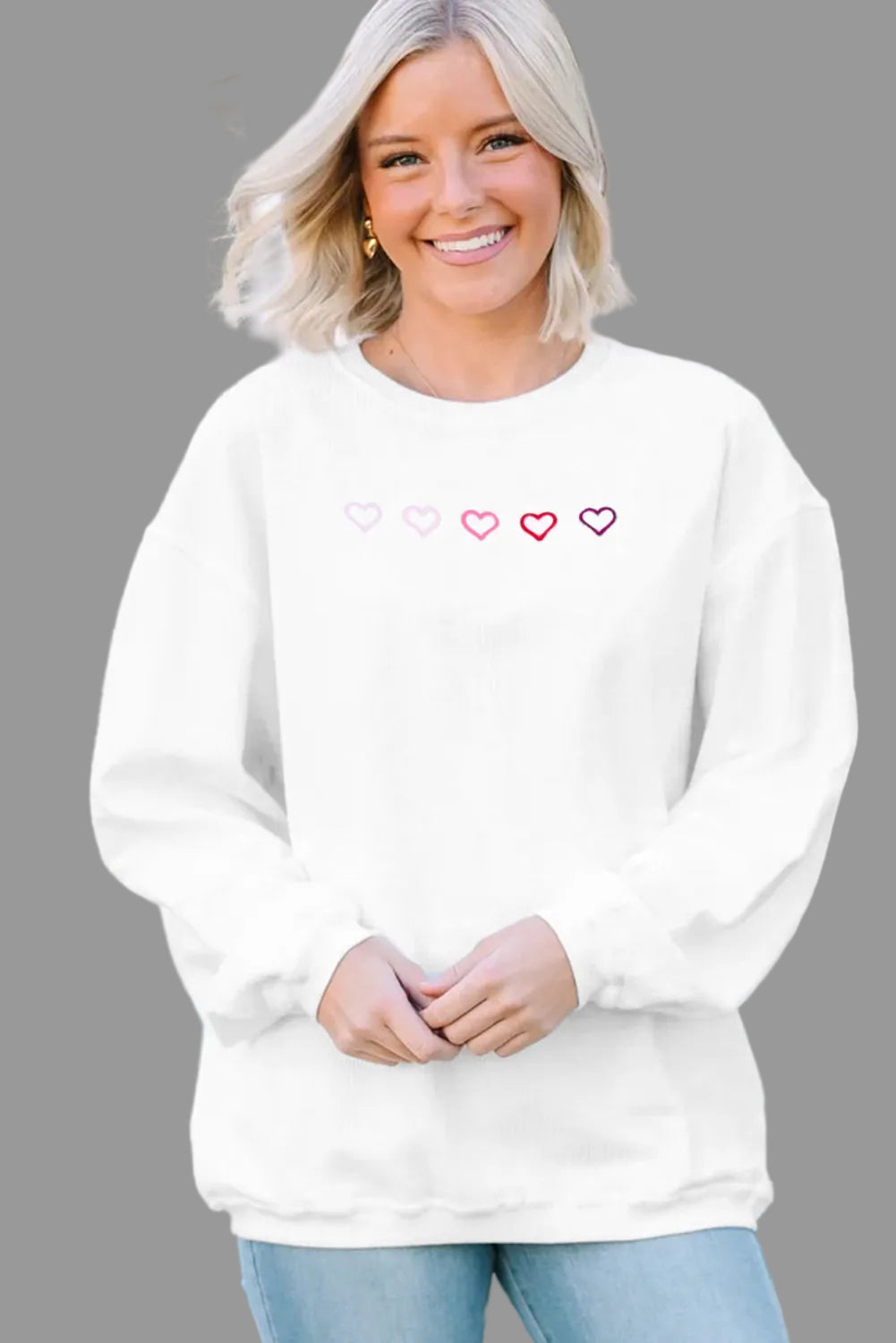 Woman wearing a white sweatshirt with heart designs in front of a white lattice background