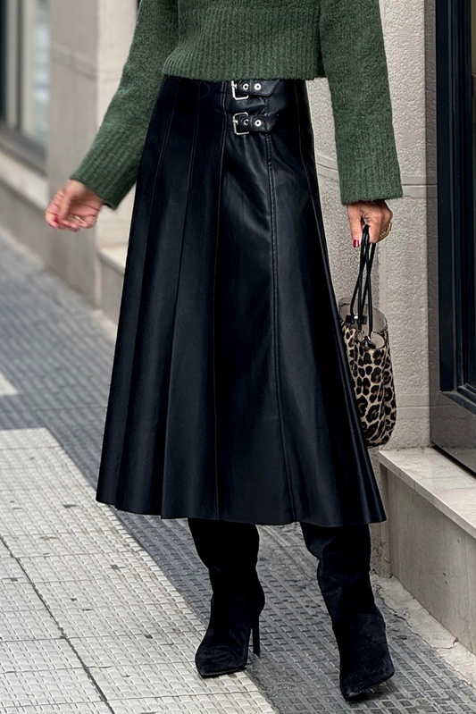 Person wearing a green sweater, black leather skirt, and black shoes on a city street.