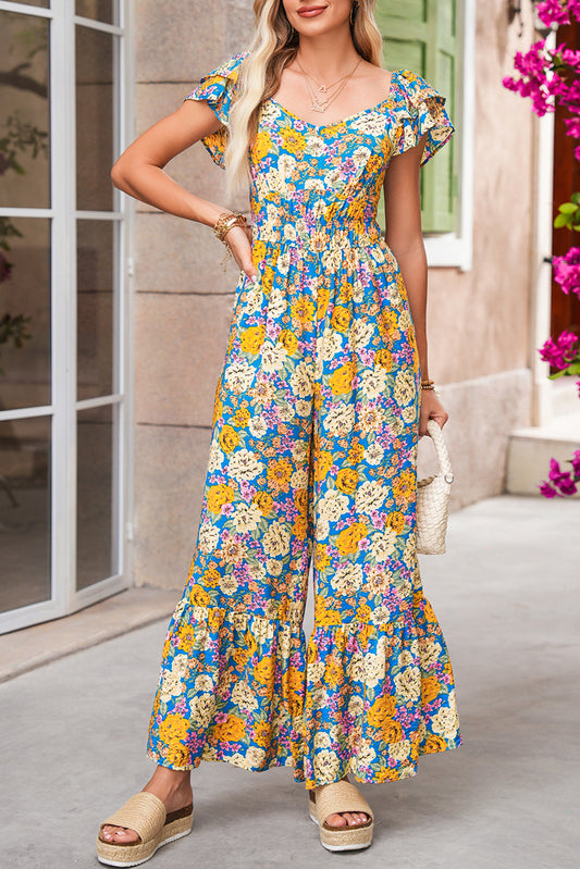 Woman wearing a colorful floral jumpsuit standing outdoors.