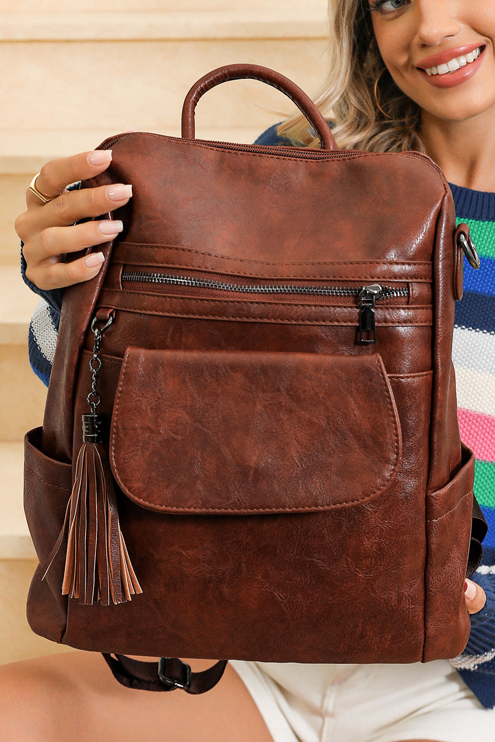 Brown leather backpack held by a person with a colorful sweater background