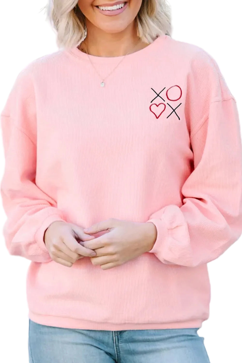 Person wearing a pink sweatshirt with a heart and cross design, standing outdoors.