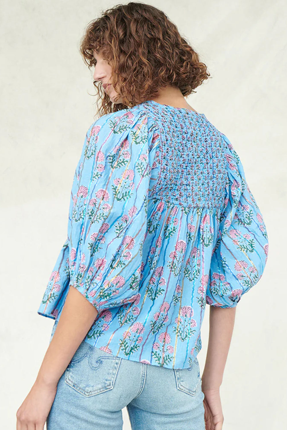 Model standing with her back turned in a light blue striped floral blouse with half sleeves.