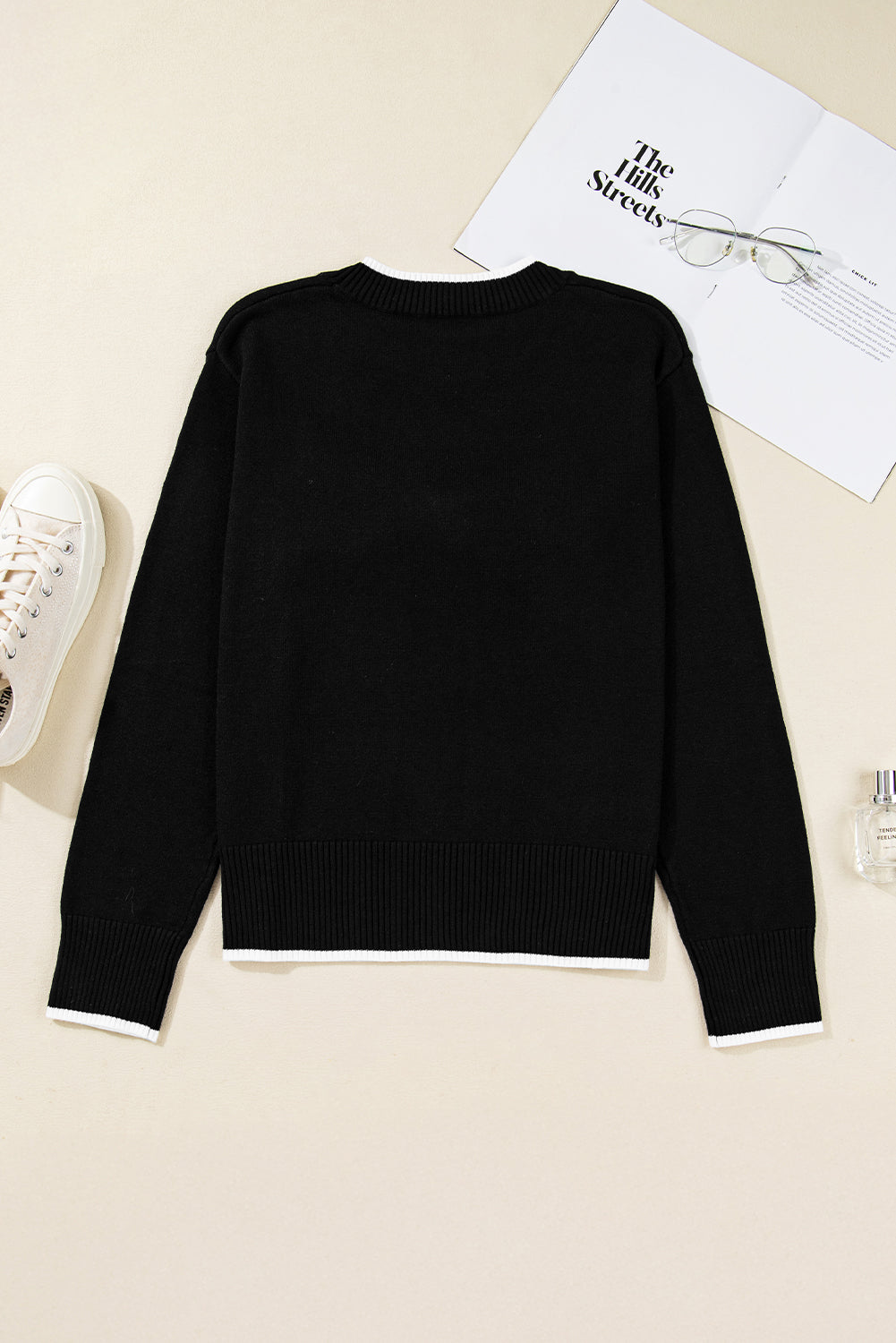 Black sweater on a beige surface with a white sneaker and paper in the background