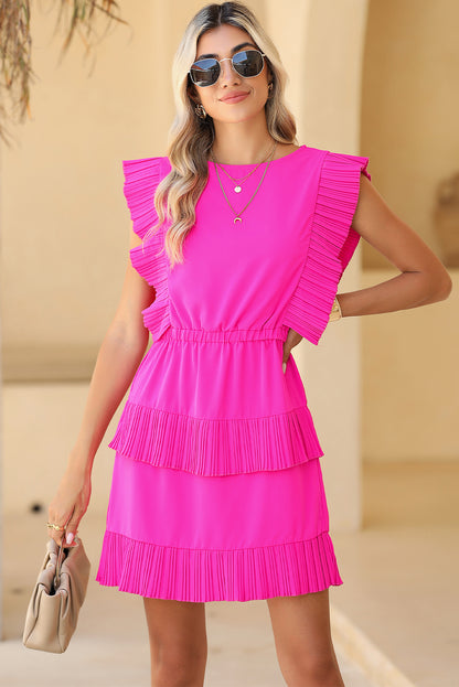 Front view of model wearing bright pink pleated layered ruffle sleeveless mini dress, sunglasses, and holding a bag in her right hand