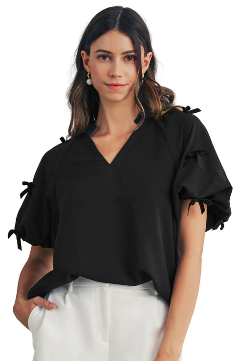 Woman wearing a black blouse with ruffled sleeves against a neutral background
