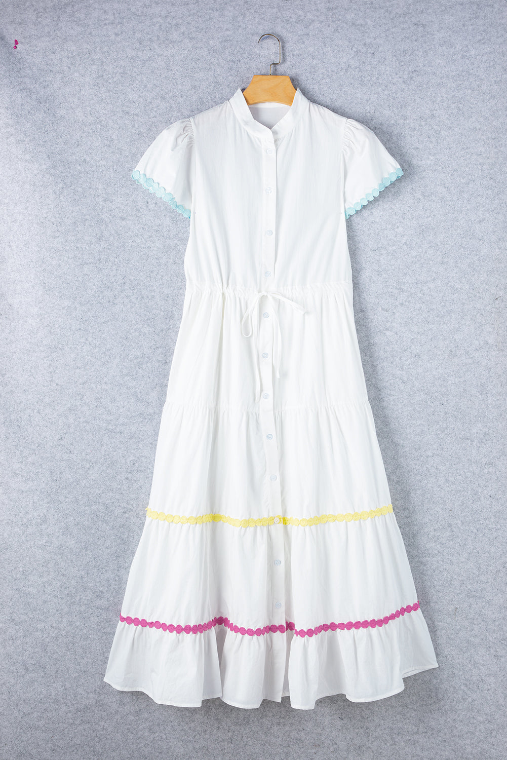 Full front view of a white tiered shirt dress with short sleeves and a waist tie displayed on a hanger, showcasing its elegant design.