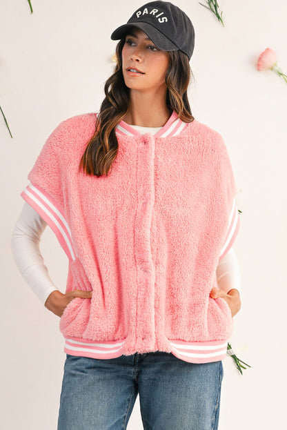 Woman wearing a pink fleece varsity jacket with white sleeves and trim, standing against a light background.