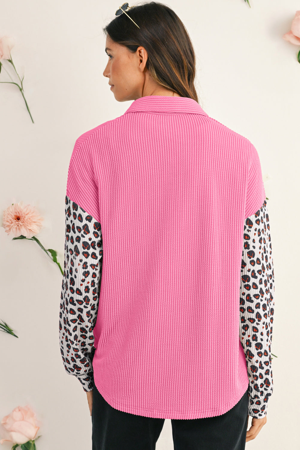 Woman wearing a pink shirt with leopard print sleeves against a light background