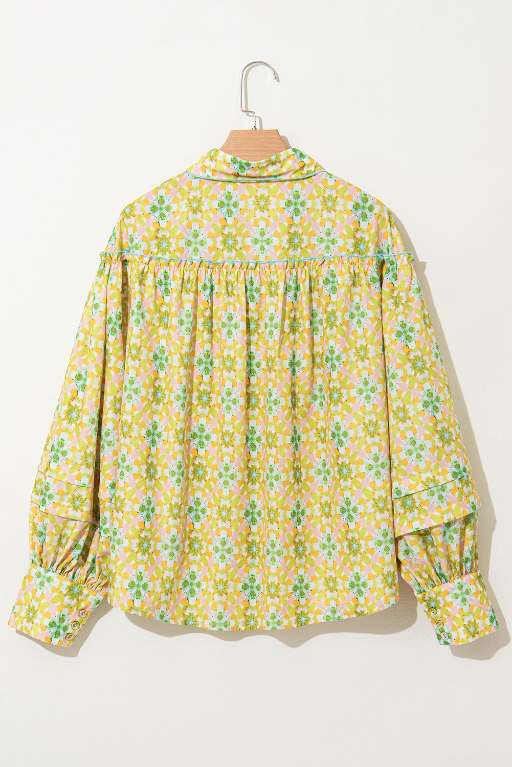 Back view of a green and yellow floral blouse with balloon sleeves on a hanger.