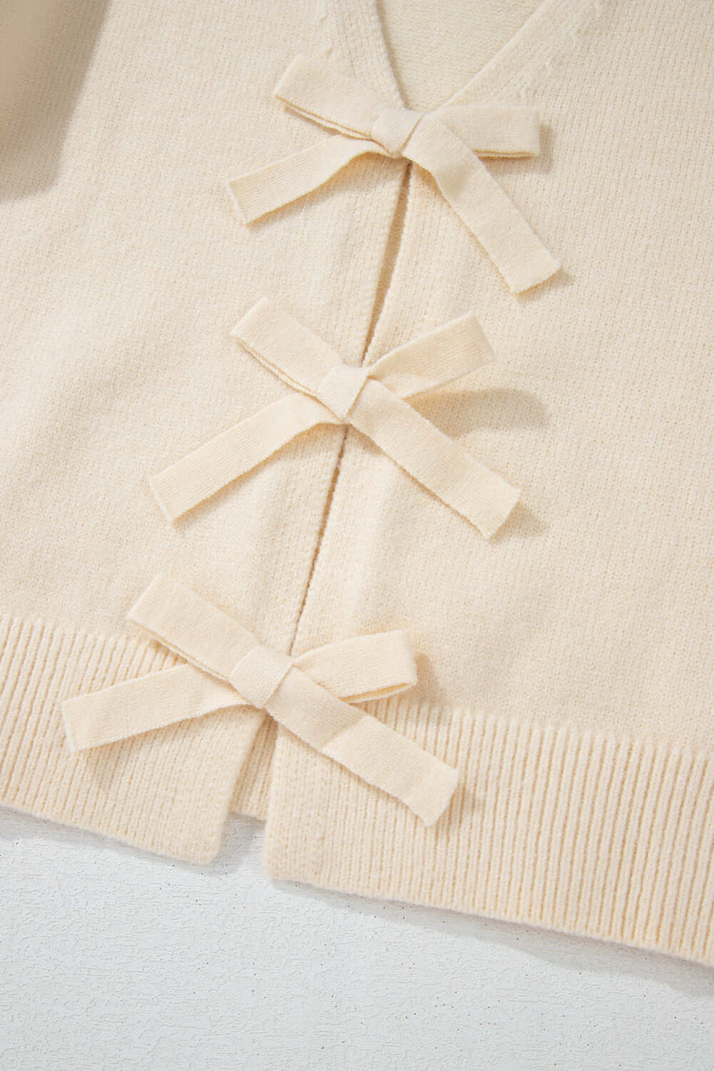 Close-up of a soft knit cardigan with delicate bow-tie details on the front.
