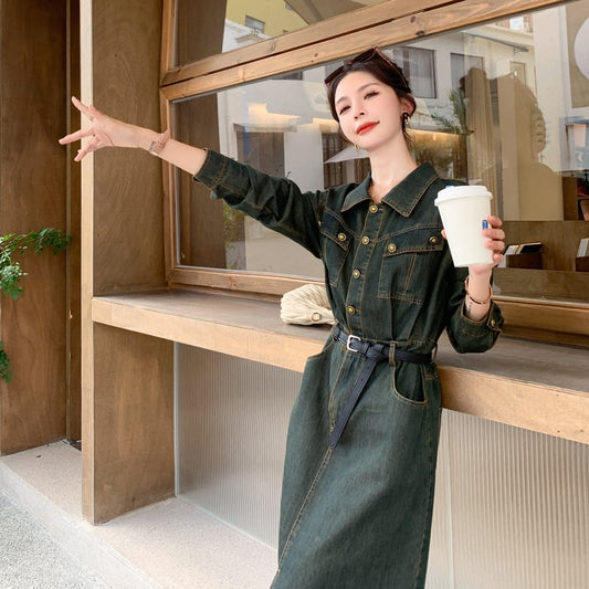 Woman in a green denim outfit holding a coffee cup in a modern interior setting.