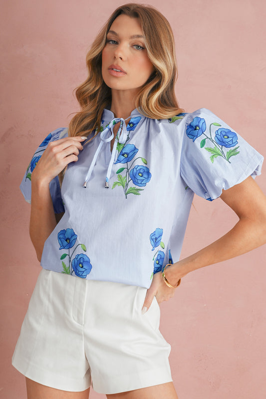 Woman wearing a light blue blouse with floral embroidery on a pink background
