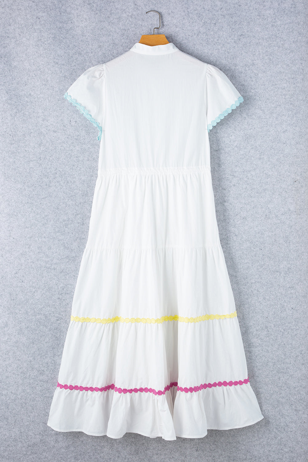 Full back view of a white tiered shirt dress with short sleeves and a waist tie displayed on a hanger, showcasing its elegant design.