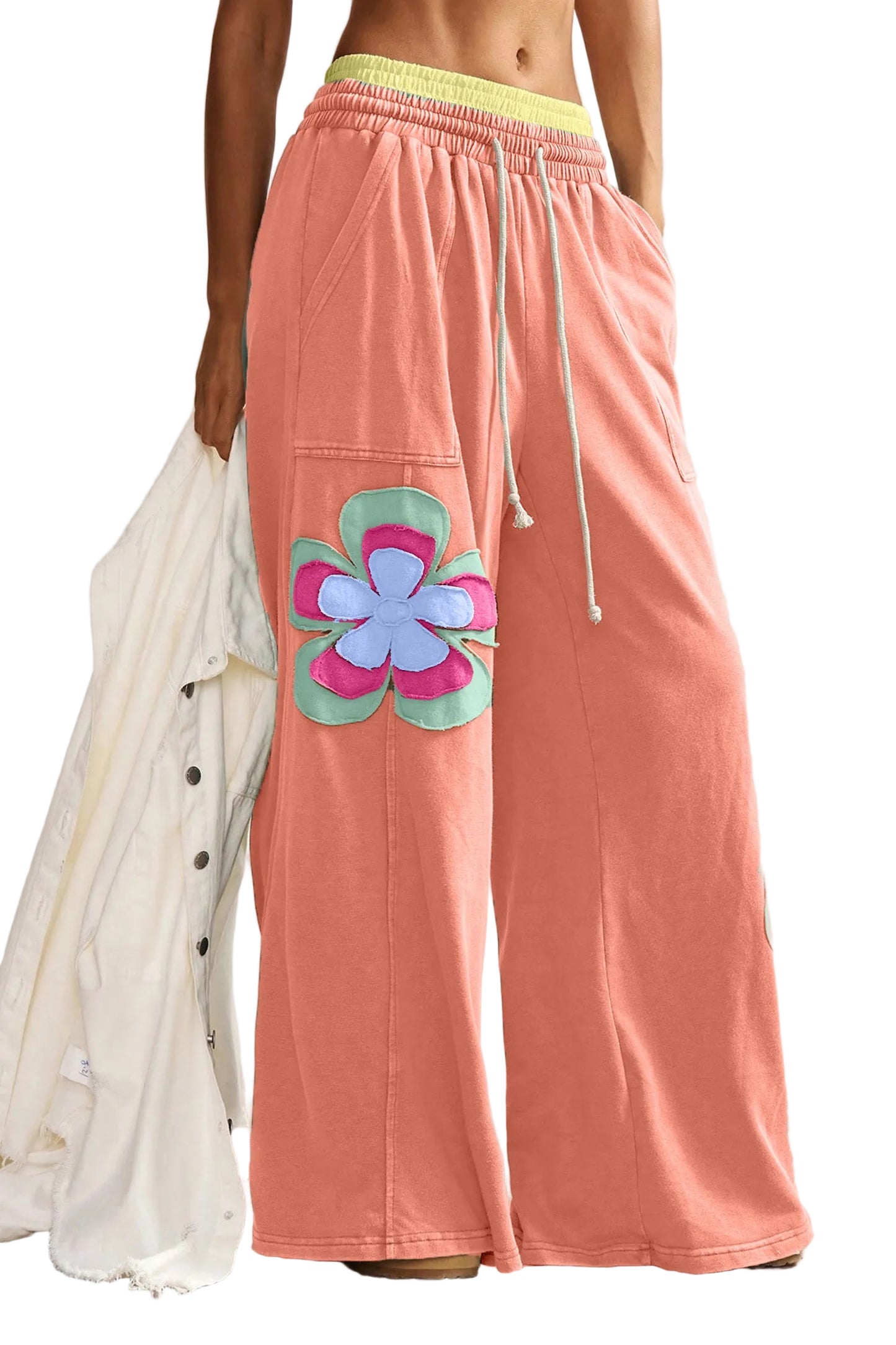 A front view of model wearing the orange wide-leg lounge pants, showcasing the oversized teal, pink, and blue floral patches and the yellow contrast waistband.