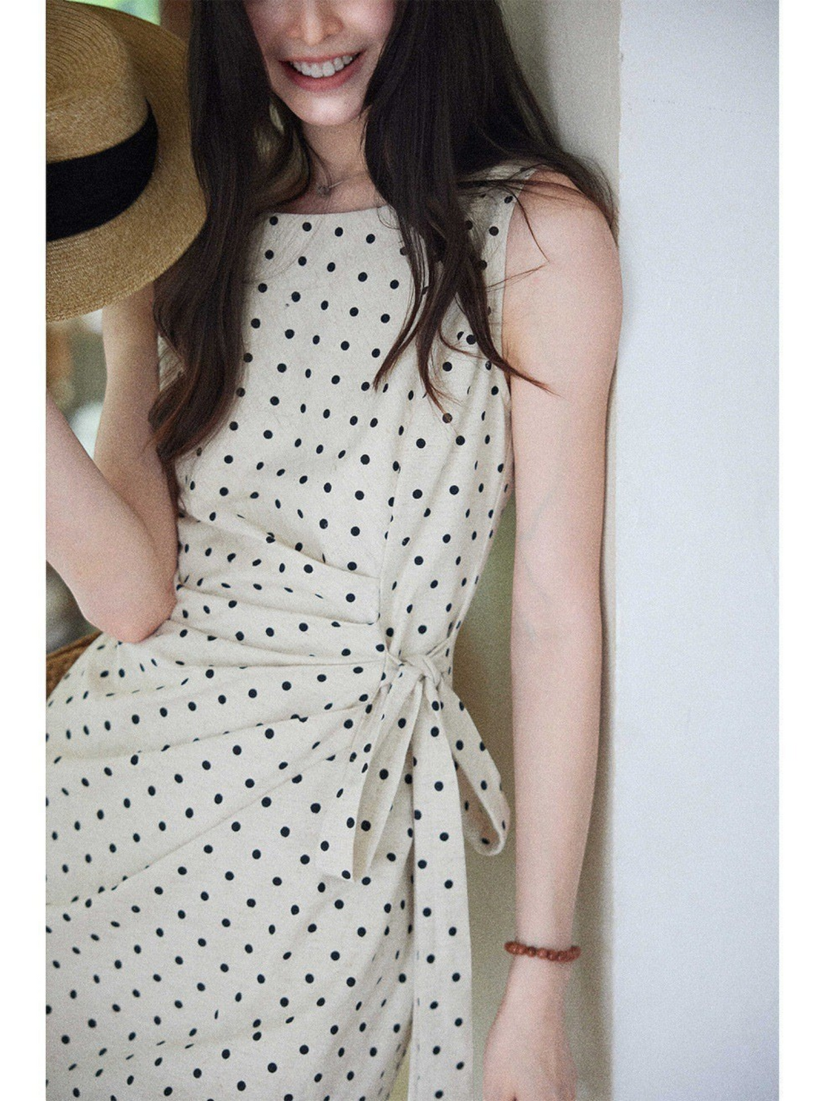 Catherine Martin sleeveless midi dress in cream linen-cotton with black polka dots and a side tie waist detail.