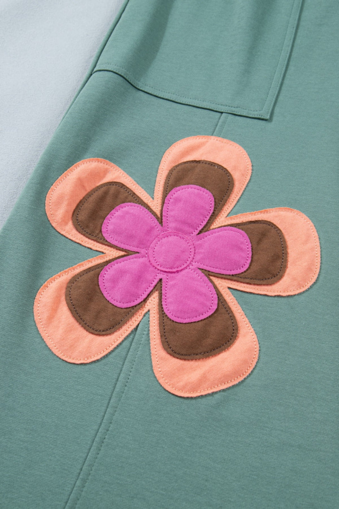 The closed-up view of the forest green patchwork wide-leg pants, highlighting the relaxed fit and the floral appliqué continuation near the right large side pocket.