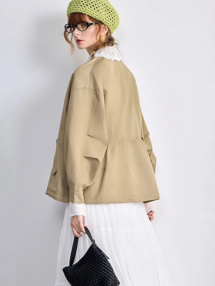 Person wearing a beige jacket, white skirt, and green beanie on a plain background