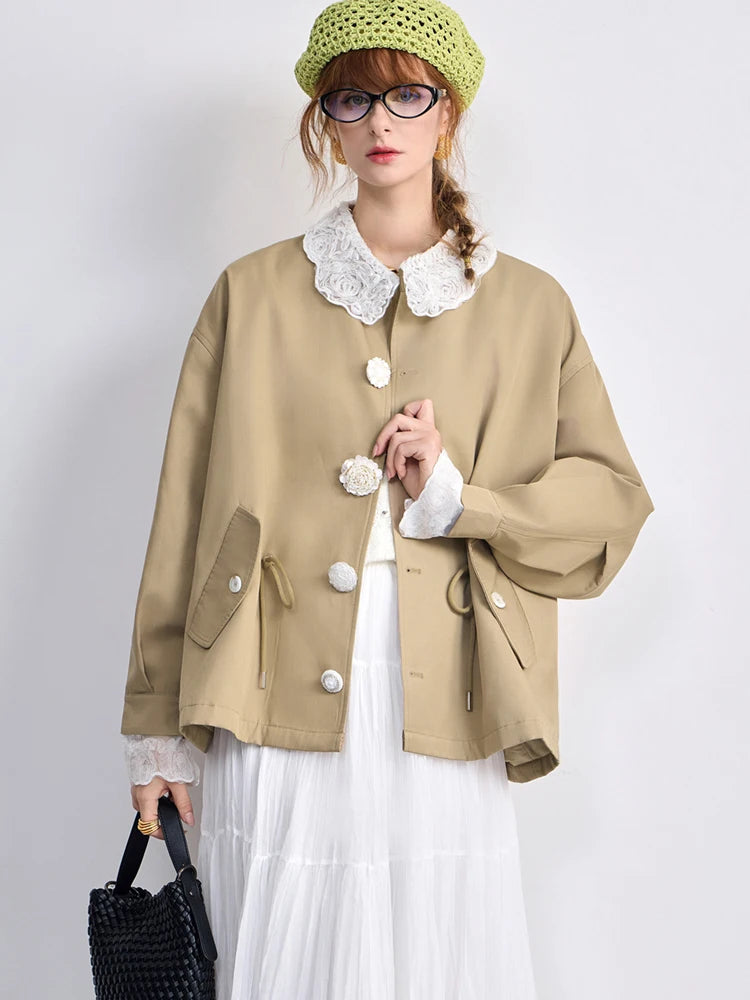 Person wearing a beige coat with a white lace collar, holding a black handbag on a white background