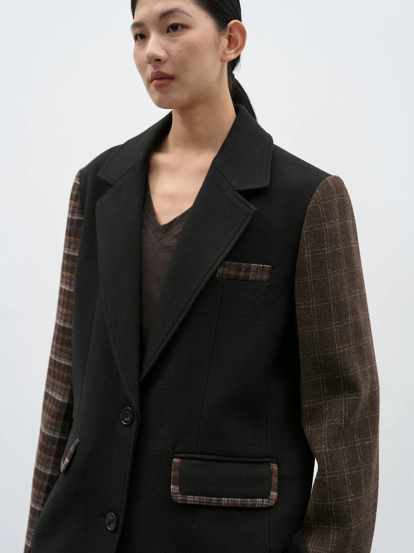 Side-profile view highlighting the sharp notched lapels and the seamless transition between the black body and plaid sleeves.
