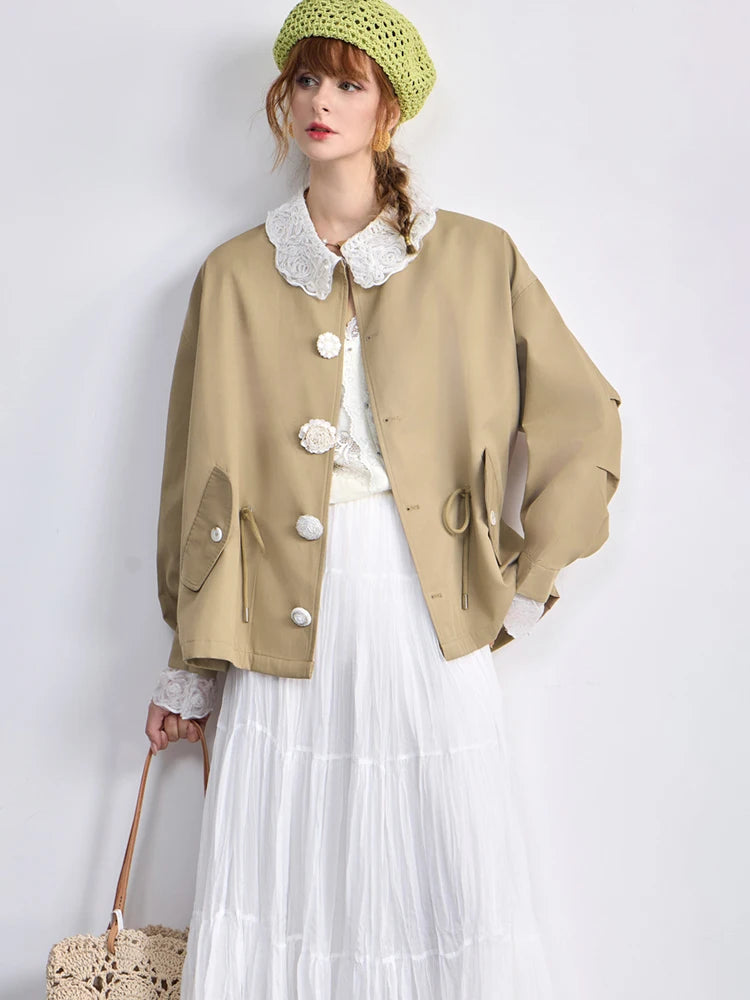 Woman wearing a beige jacket with white details, white skirt, and green hat on a plain background
