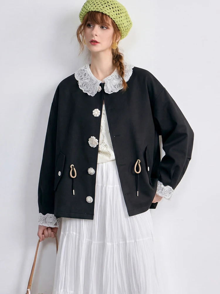 Woman wearing a black jacket with white lace details on a plain background