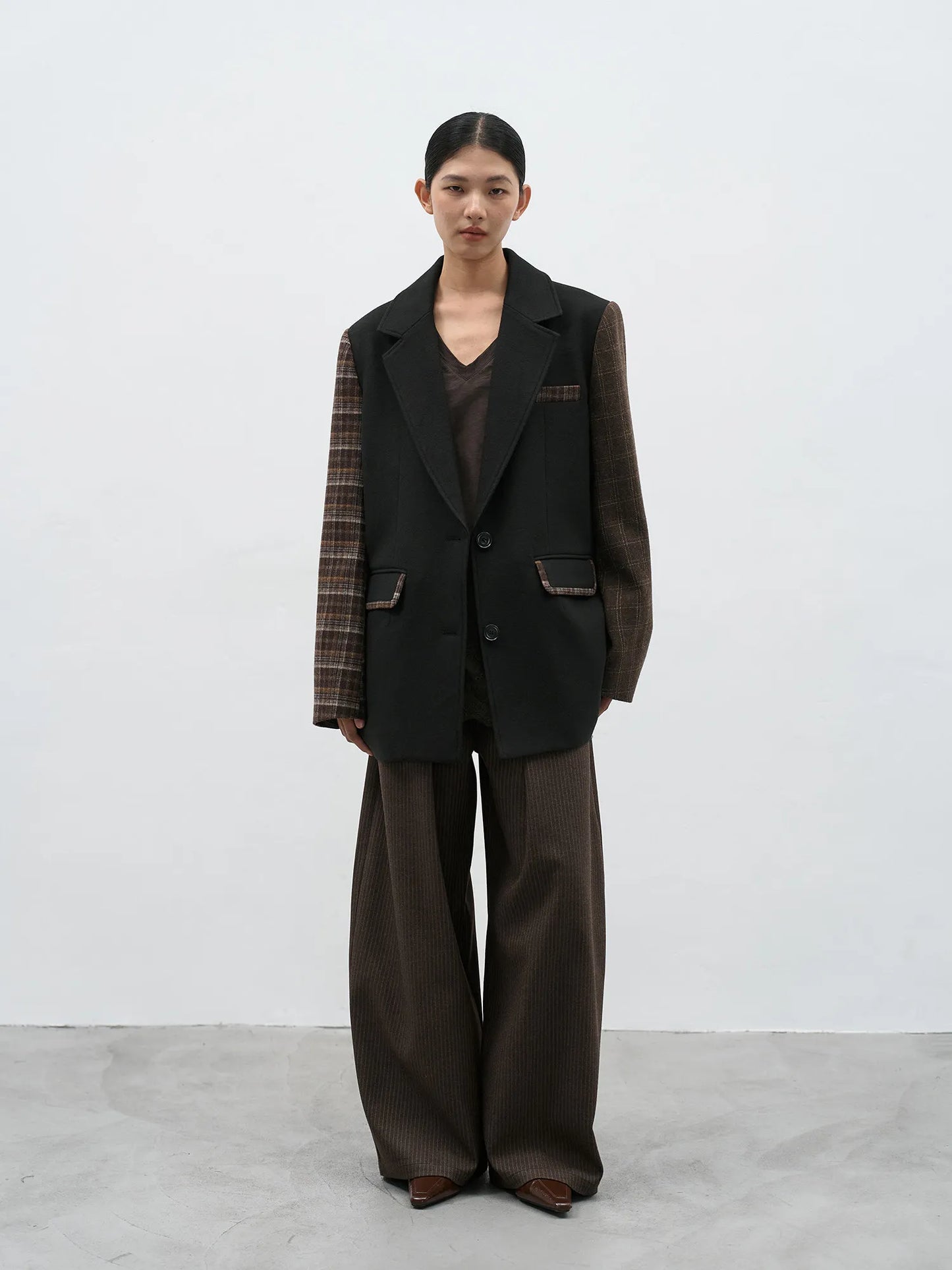 Front view of a women's oversized black wool-blend blazer with brown plaid patchwork sleeves and a loose fit.