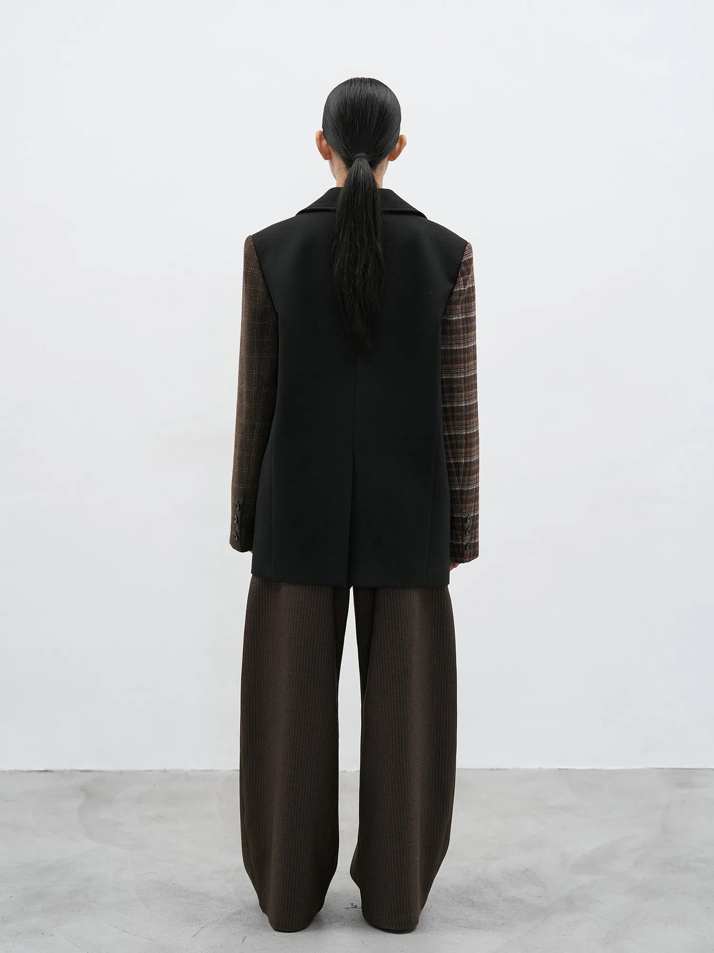 Rear view of the patchwork blazer showing the clean black woolen back and the contrast plaid sleeve detail.