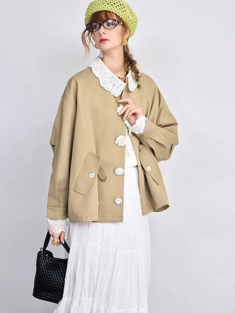 Woman wearing a beige coat with white lace details on a plain background