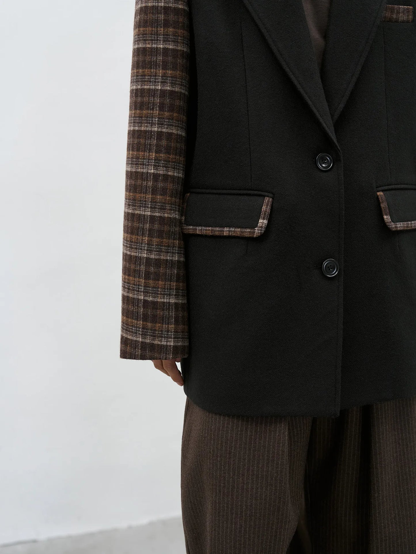 Close-up of the functional flap pocket featuring a sophisticated brown plaid trim on a black woolen base.