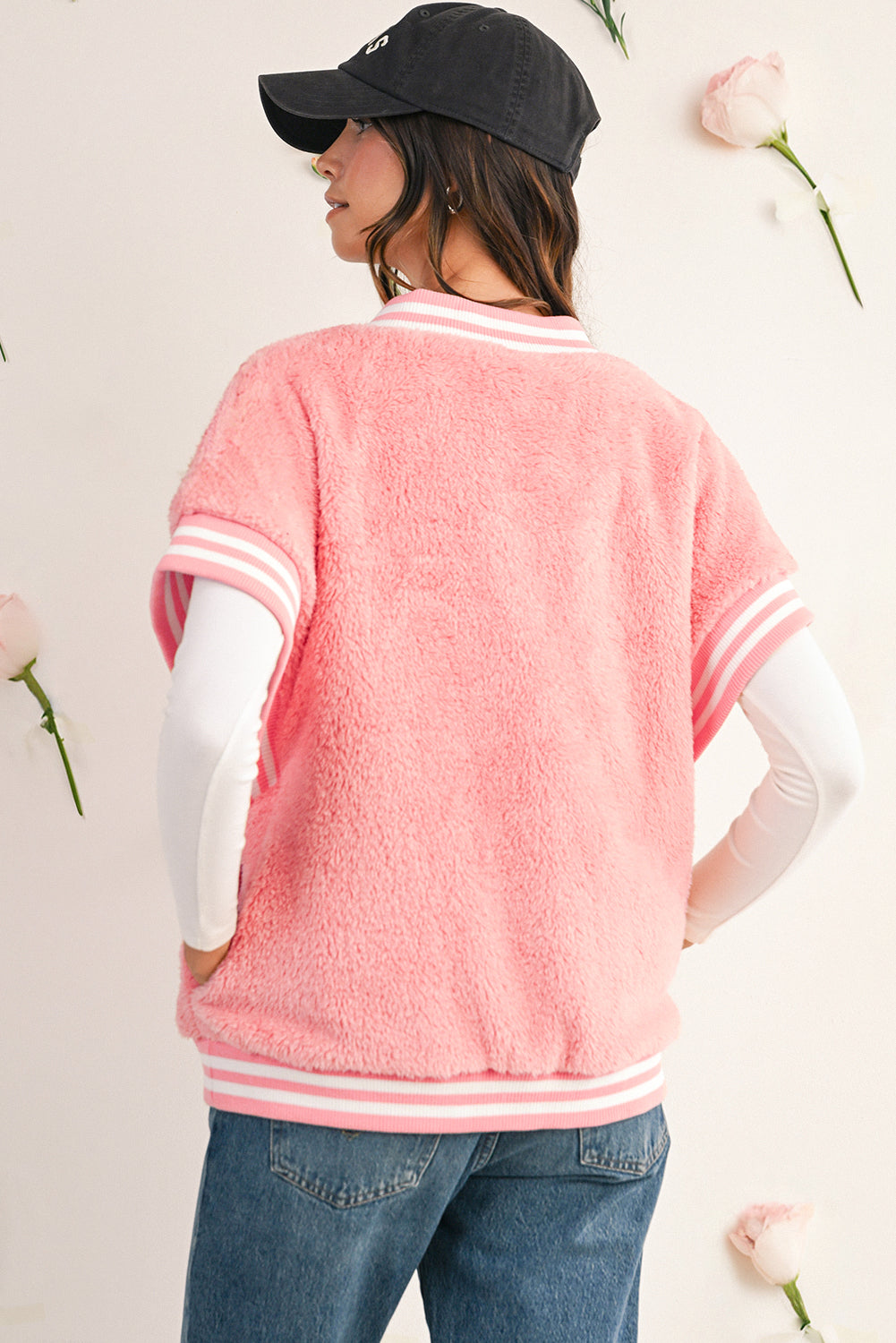 Person wearing a pink varsity jacket with white accents, standing against a light background with flowers.