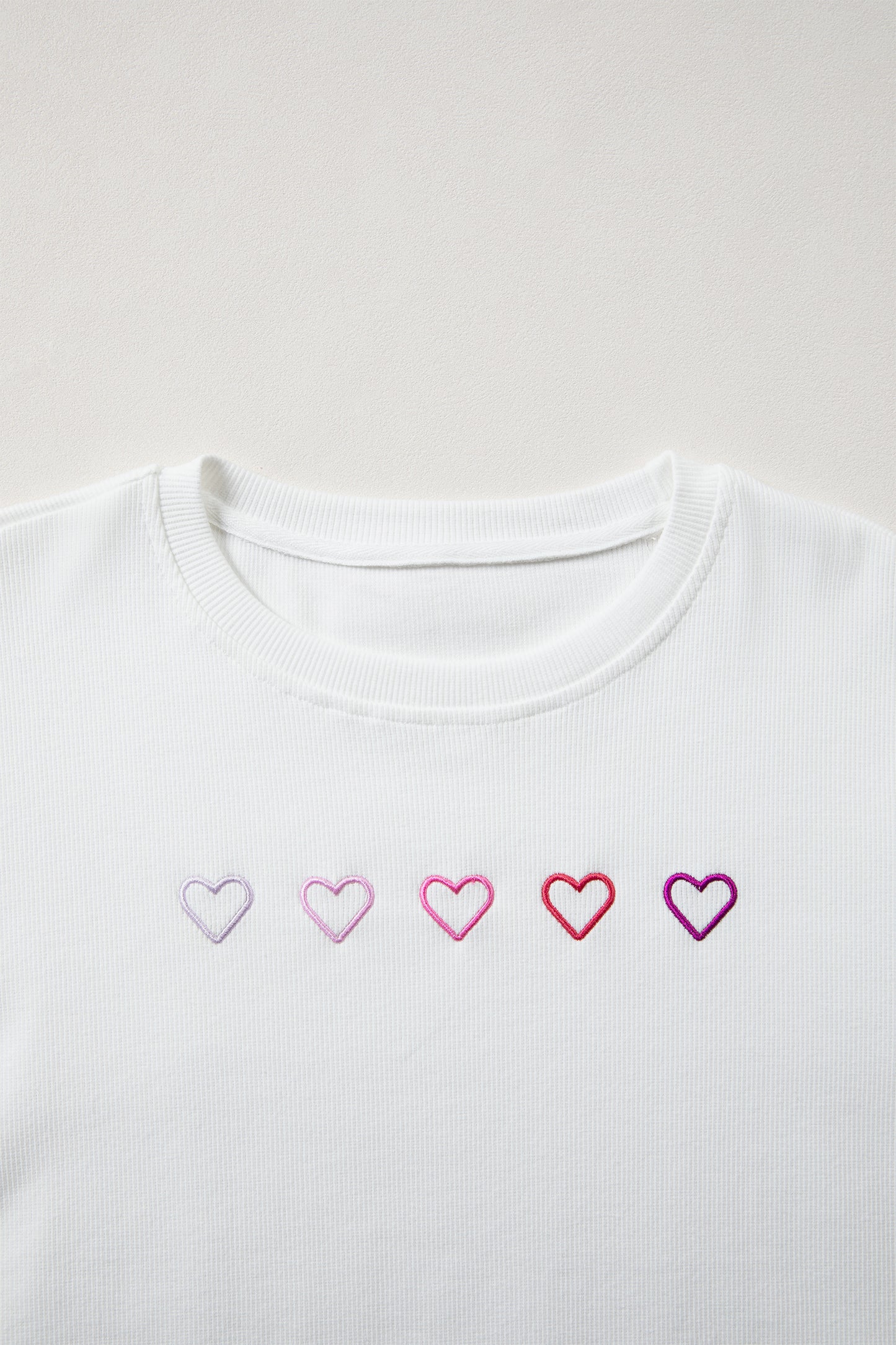 White t-shirt with embroidered hearts on a light gray background
