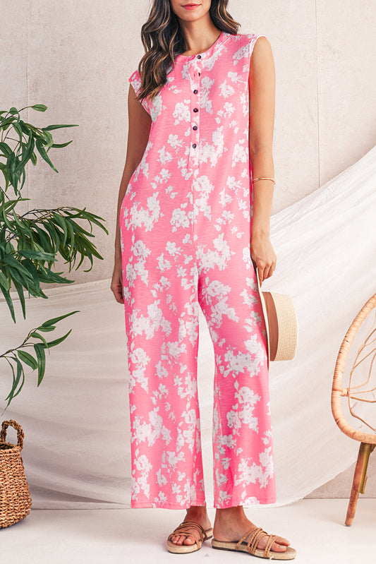 Woman wearing a pink floral jumpsuit with a plant and chair in the background