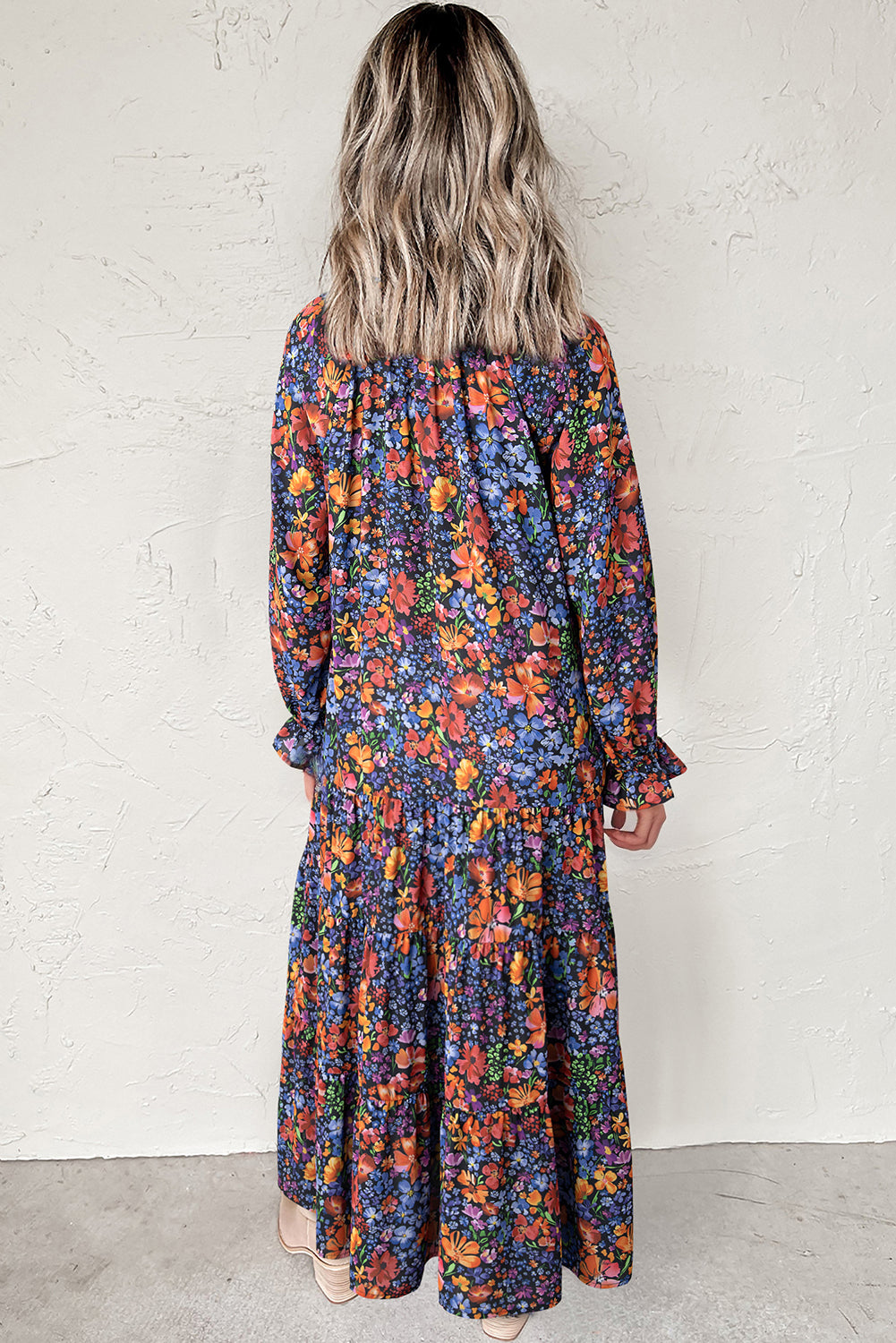 Person wearing a colorful floral dress against a white wall.
