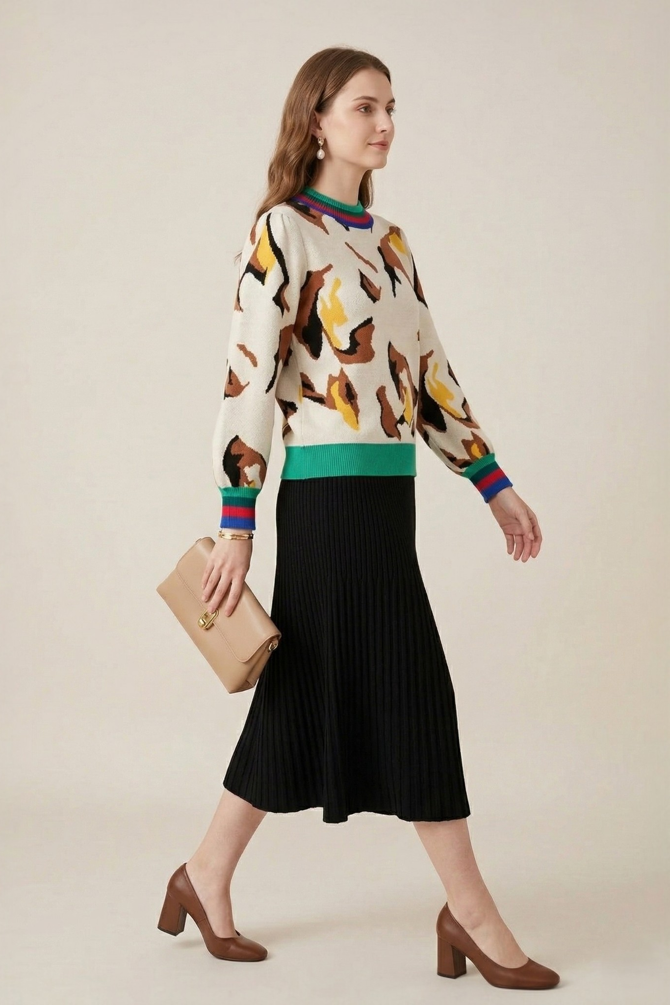 Abstract print stripe trim knit sweater side view model walking with beige clutch styled with black pleated midi skirt and brown block heels