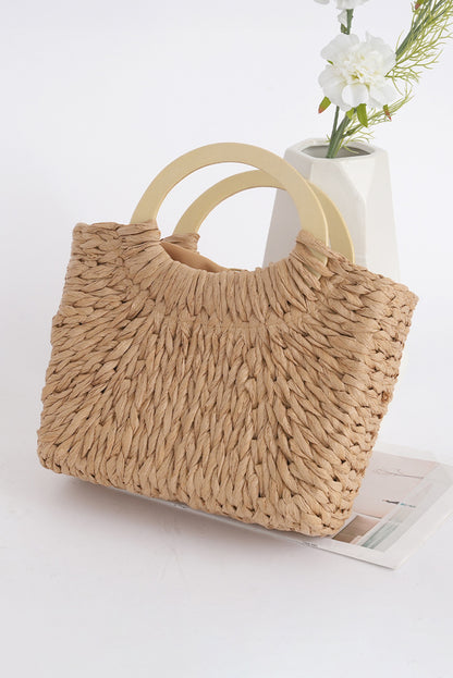 Beige woven handbag with wooden handles on a white surface with a vase of flowers in the background.