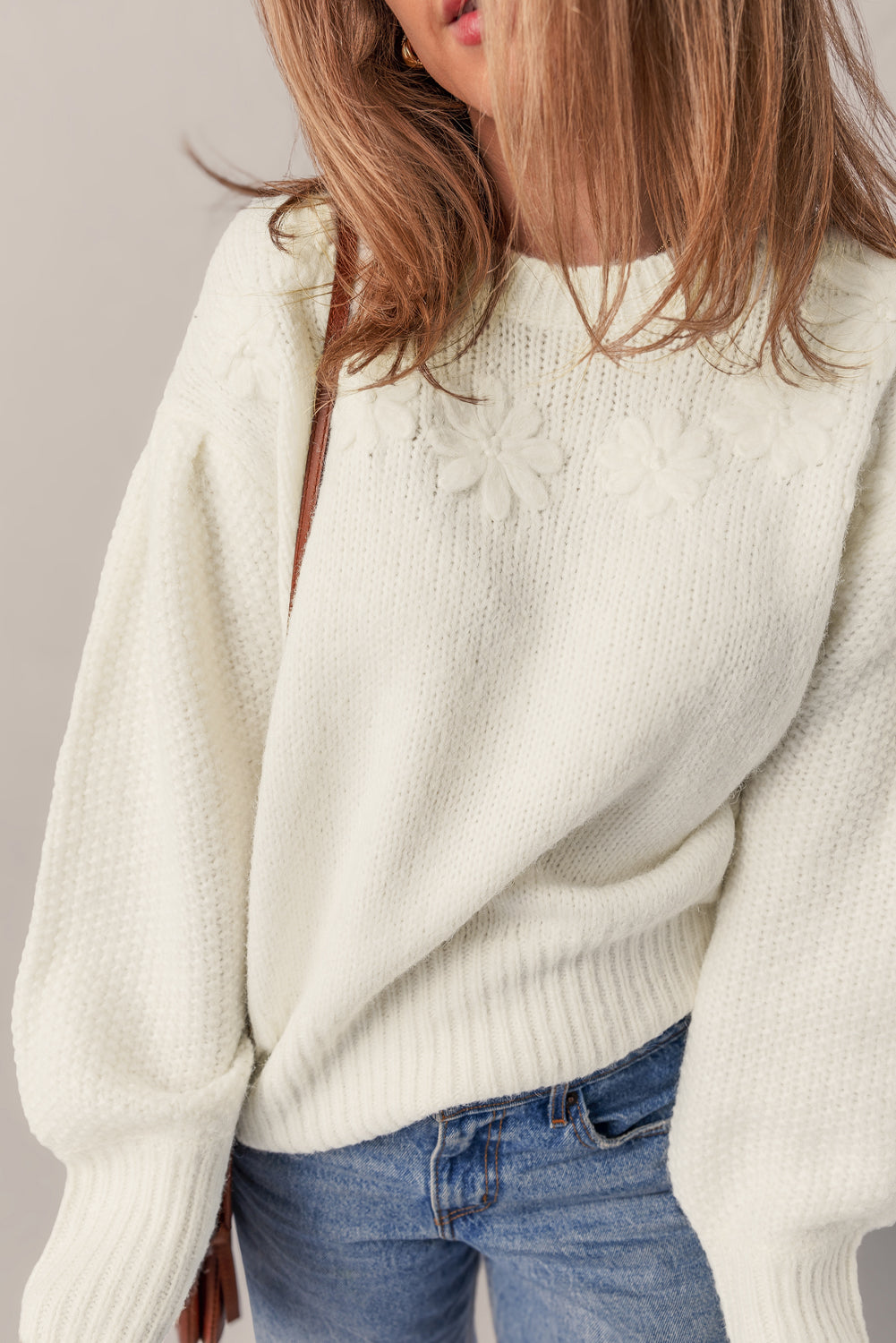Person wearing a white sweater and blue jeans against a neutral background