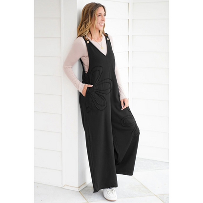 Woman wearing a black jumpsuit leaning against a wall.