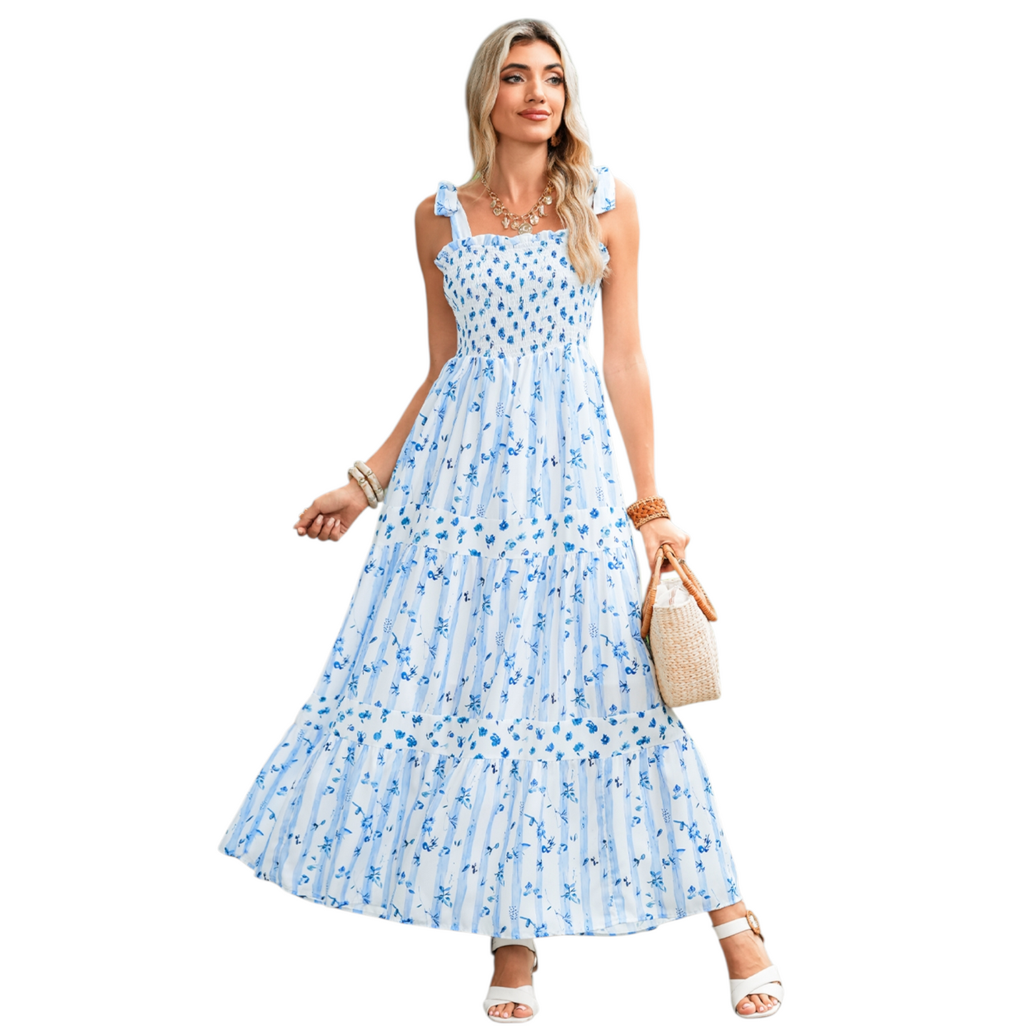 A woman wearing a blue and white striped maxi dress with a floral print, featuring a shirred bodice, tie-up ribbon shoulder straps, and a tiered flowy skirt.
