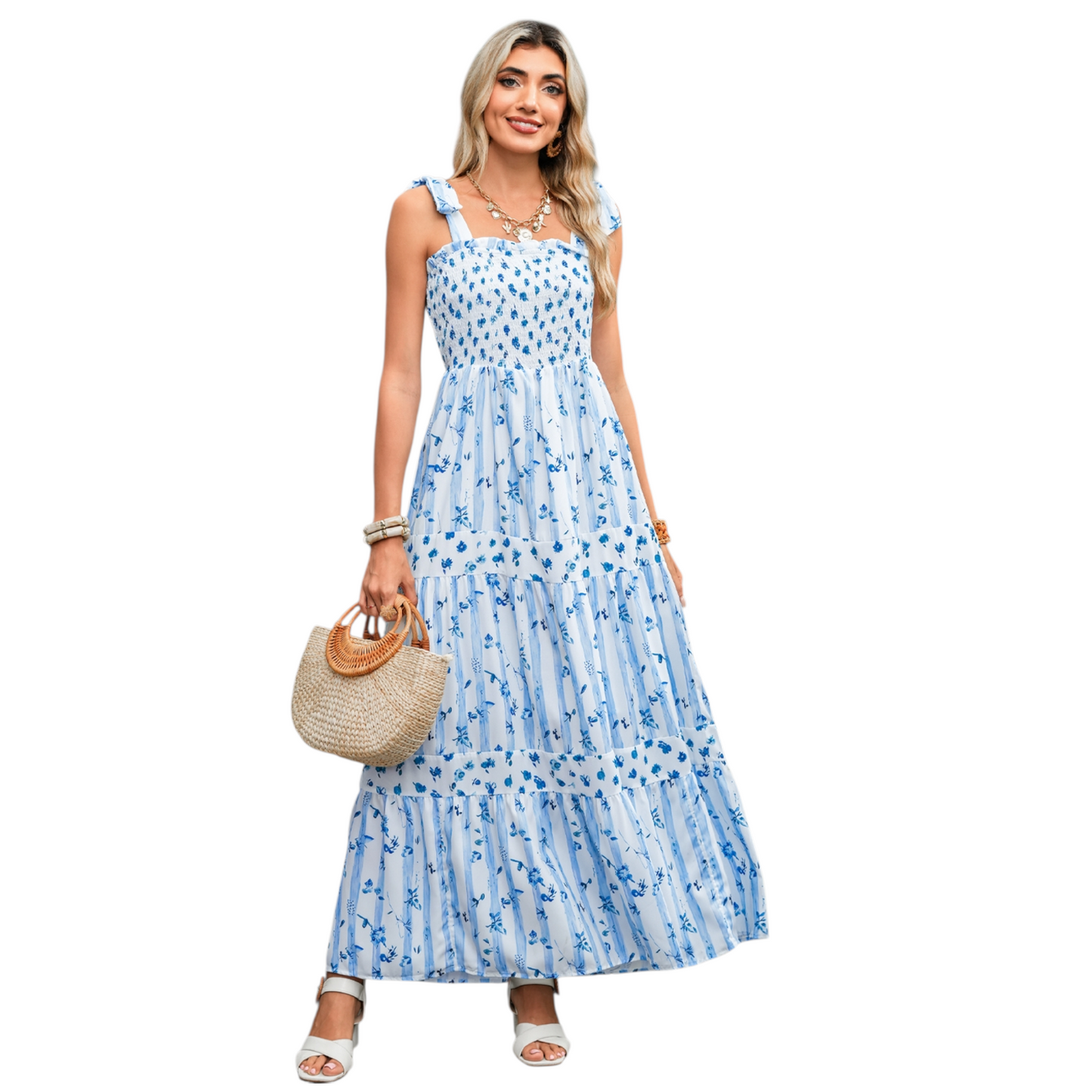 A woman wearing a blue and white striped maxi dress with a floral print, featuring a shirred bodice, tie-up ribbon shoulder straps, and a tiered flowy skirt.