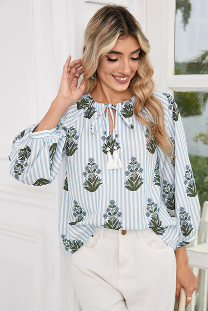 Front view of a blue floral striped blouse with long sleeves and tie neckline, perfect for spring and summer, worn by a model paired with white pants from Catherine Martin store.